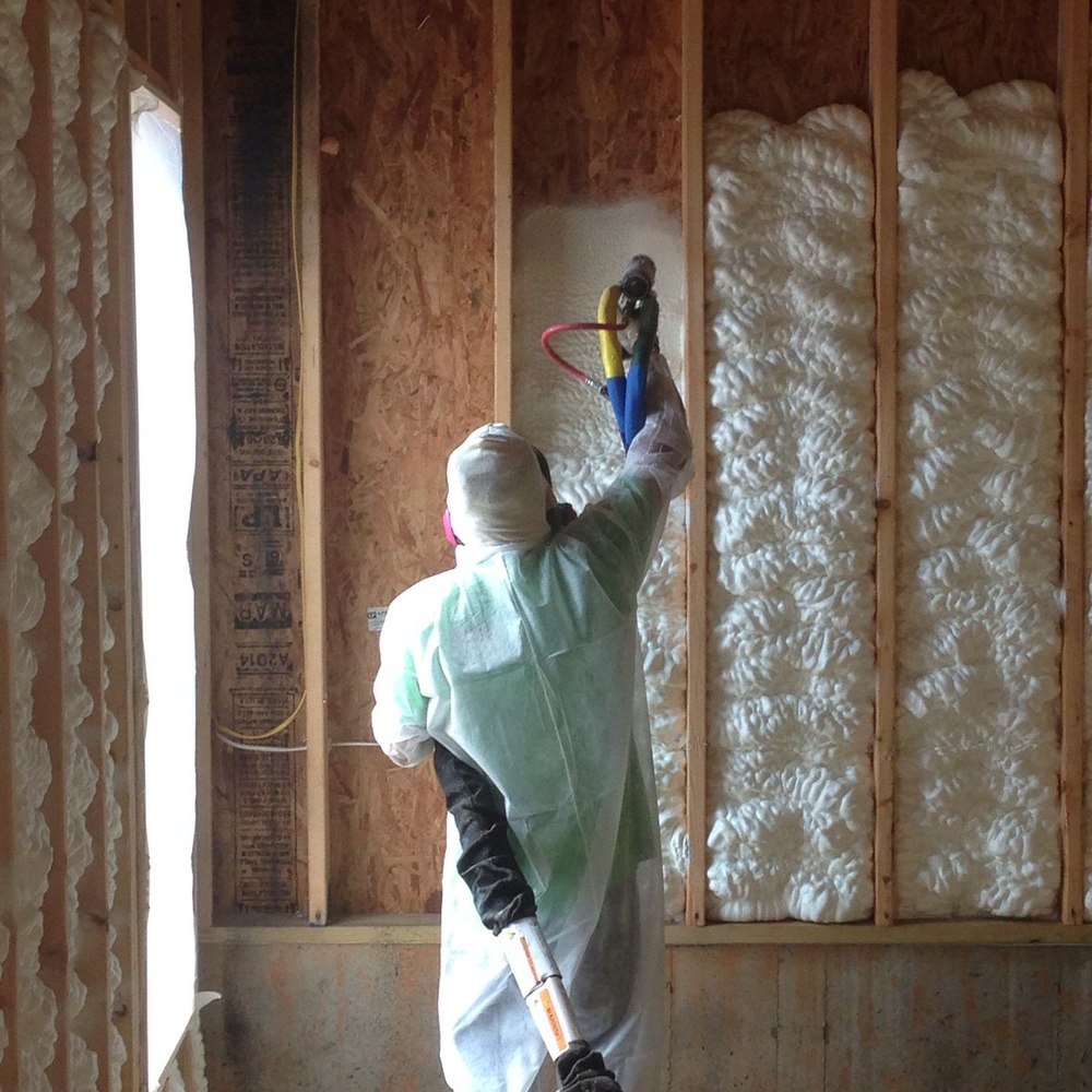 Technician spray-foaming insulation into a wall cavity to seal the building envelope